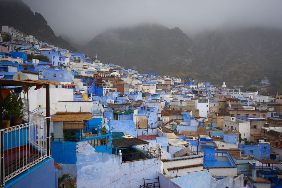 Blue and white houses crowding up a hillside, under mountains half lost in low cloud.