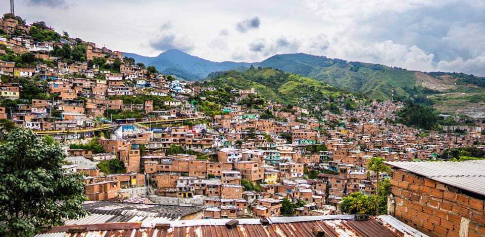 Brick houses stacked up a hillside as far as the eye goes, with green mountains behind and rusted tin roofs in the foreground.