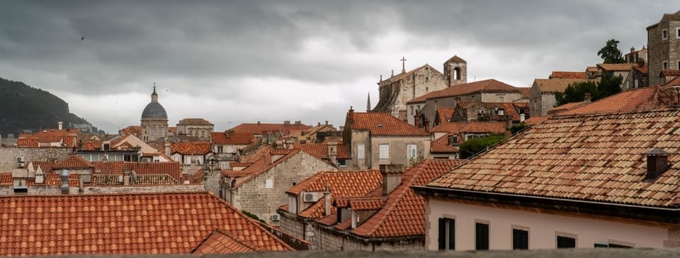 Terracotta roofs, stone bell towers and a dome under heavy grey cloud.