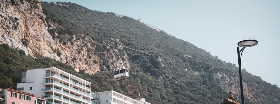 A cable car climbing the scrub-covered face of the Rock, above white apartment blocks.