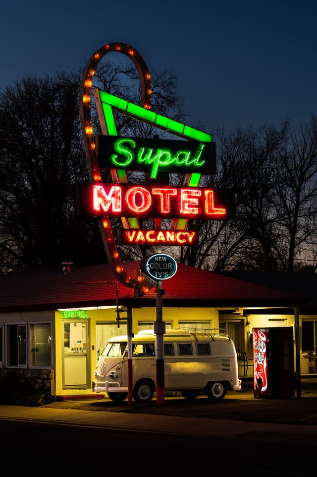 The Supai Motel’s neon sign lit green and red at dusk, with a cream Volkswagen bus parked under it.
